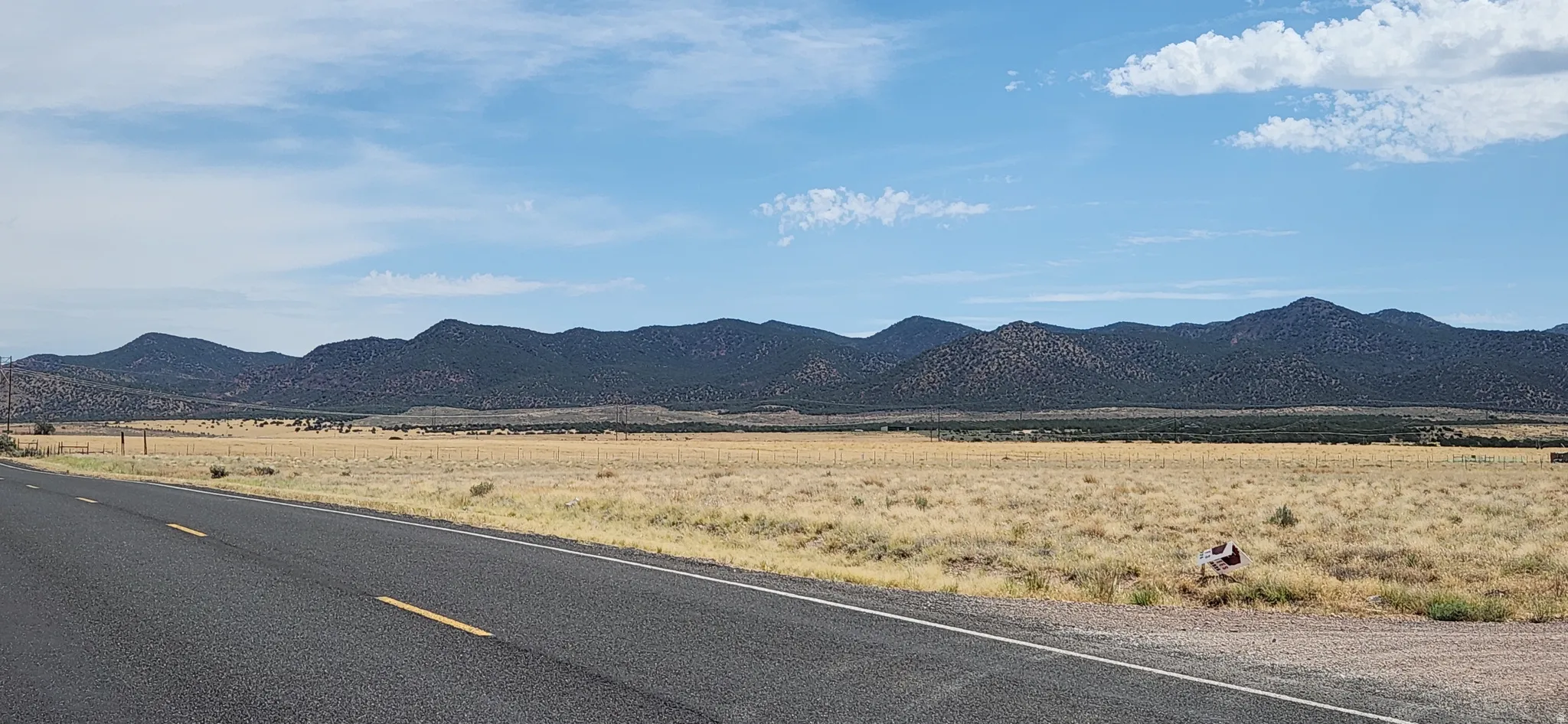 Paved road with double yellow lines, extensive open terrain, and distant mountains