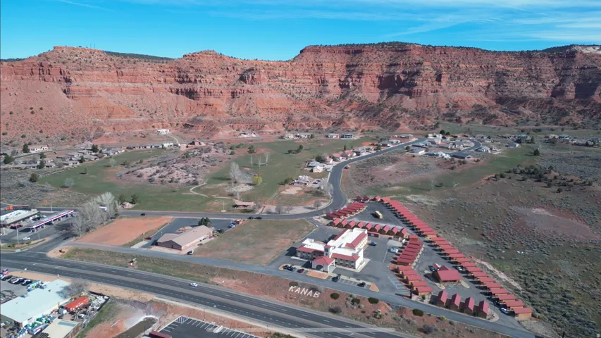 Expansive red rock geological formations, commercial buildings, paved roads, and developed land with a "KANAB" sign