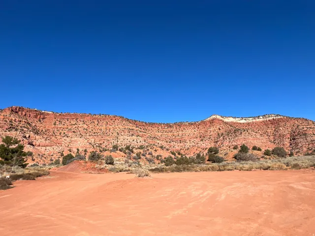 Expansive red earth landscape with distant red rock formations and scattered desert vegetation