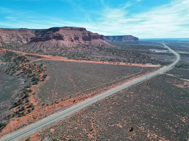 Expansive desert landscape featuring a paved road, red rock formations, and scattered vegetation