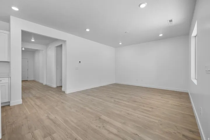 Spacious open living area with warm wood-finish flooring throughout, recessed ceiling lighting, and clean white walls