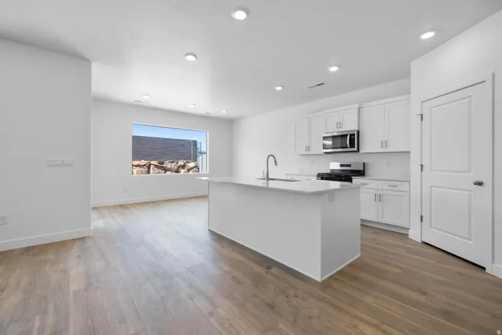 Open-concept kitchen with white cabinetry, stainless steel appliances, a central island with a sink, and recessed lighting