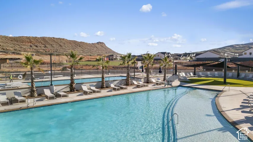 Expansive swimming pool with integrated lazy river, surrounded by a paved deck with multiple lounge areas, mature palm trees, and shade structures