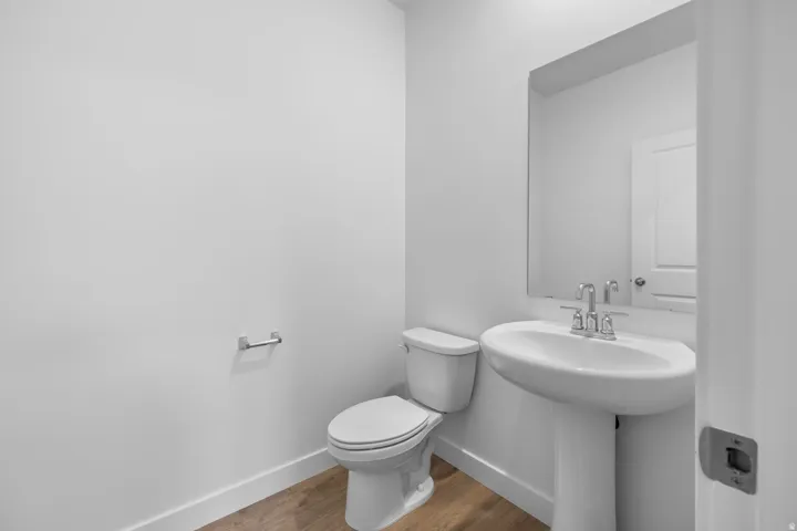 Pedestal sink with chrome faucet, wall-mounted mirror, toilet, and wood-finish flooring
