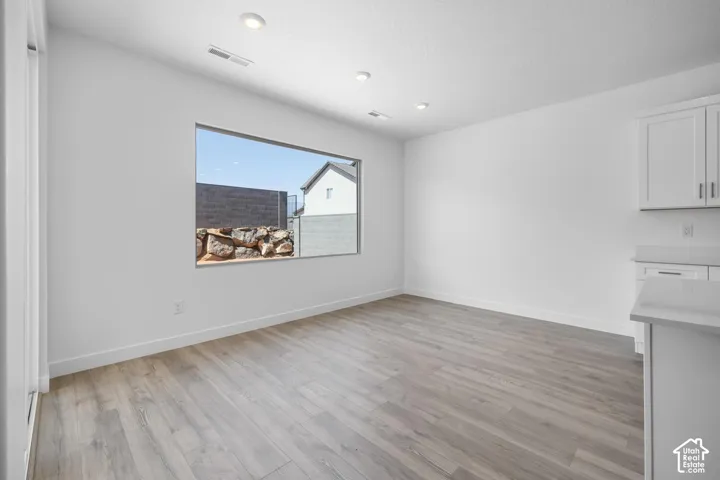 Bright, open room showcasing wood-finish flooring, recessed ceiling lighting, and a large window framing natural light