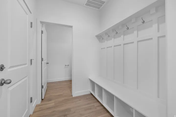 Bright mudroom featuring custom white shaker-style wall paneling with integrated cubbies, polished chrome hooks, wood-finish flooring, and direct access to multiple interior spaces