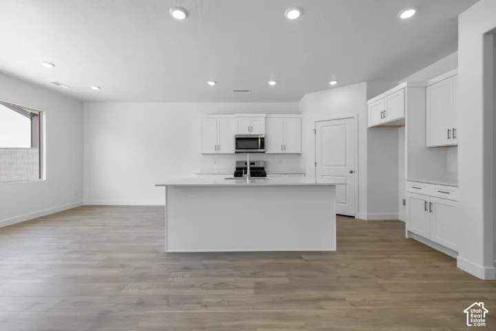 Modern kitchen featuring white cabinetry with stainless steel appliances, a large island with seating space, recessed ceiling lighting, and wood-finish flooring throughout the open-concept layout