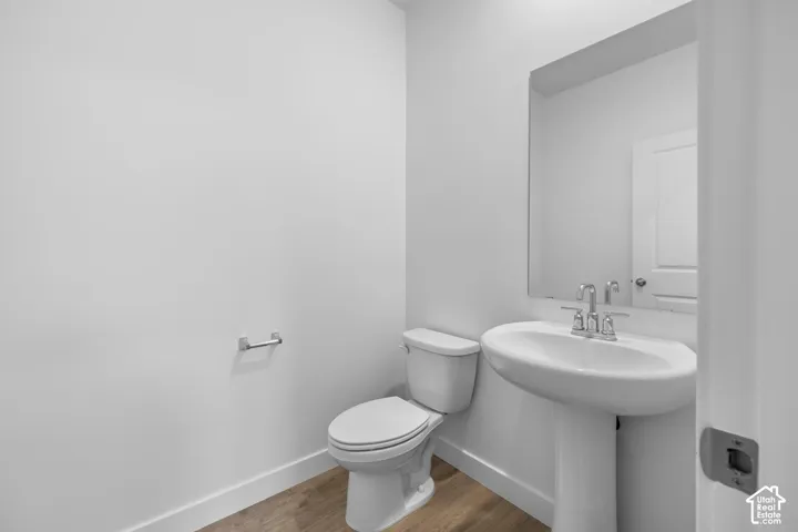 Pedestal sink with chrome faucet, wall-mounted mirror, toilet, and wood-finish flooring