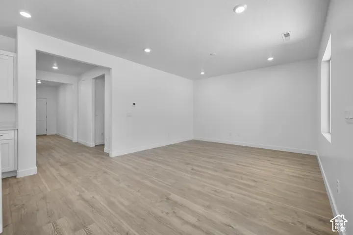 Spacious open living area with warm wood-finish flooring throughout, recessed ceiling lighting, and clean white walls