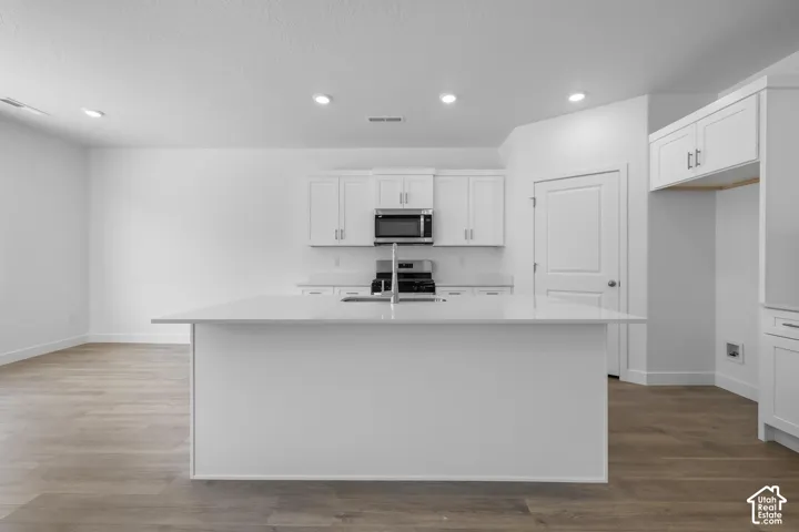 Modern kitchen featuring white cabinetry with stainless steel appliances, a large center island with waterfall countertop, recessed ceiling lighting, and wood-finish flooring throughout the open-concept space
