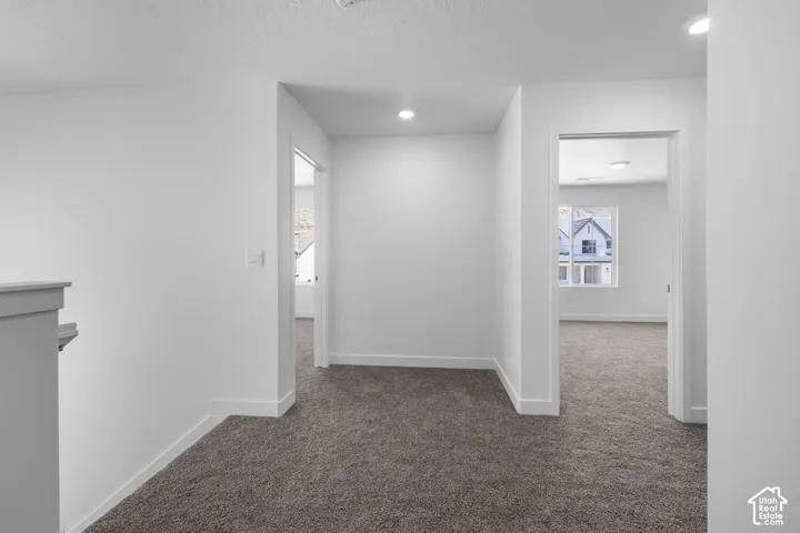 Bright hallway with recessed lighting and clean white walls opening to multiple rooms