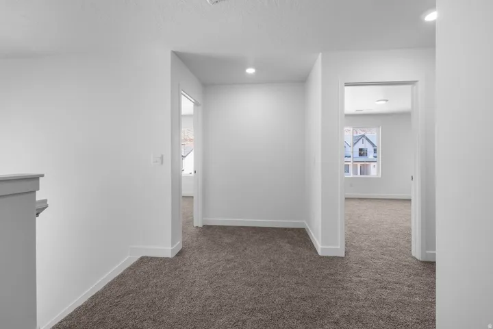 Bright hallway with recessed lighting and clean white walls opening to multiple rooms