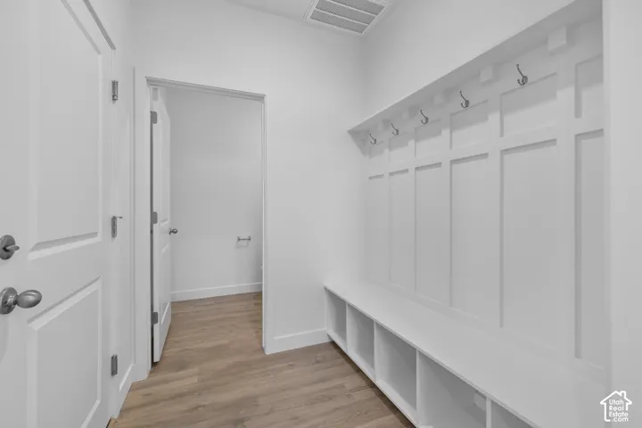Bright mudroom featuring custom white shaker-style wall paneling with integrated cubbies, polished chrome hooks, wood-finish flooring, and direct access to multiple interior spaces