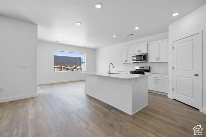 Open-concept kitchen with white cabinetry, stainless steel appliances, a central island with a sink, and recessed lighting