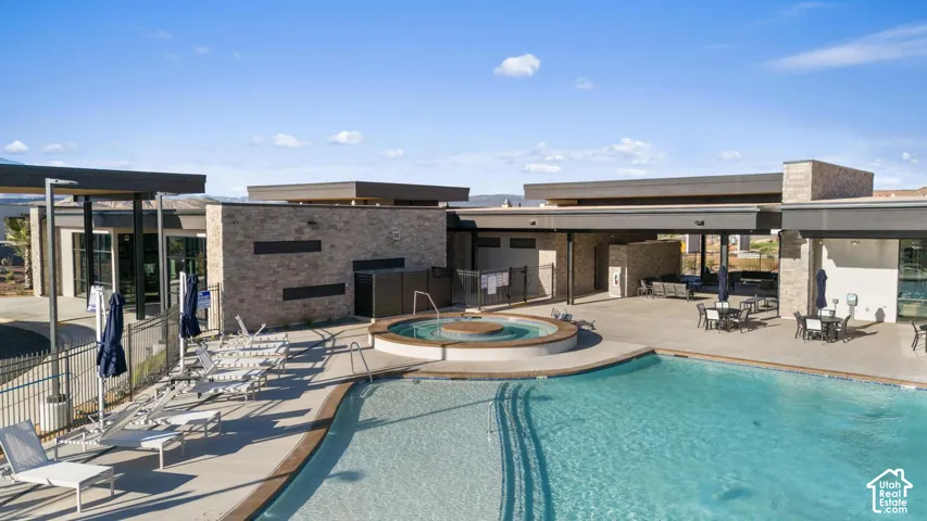 Resort-style outdoor living featuring a sparkling lagoon-form swimming pool with integrated spa, expansive sun deck with lounge seating areas, and contemporary single-story residential structures with clean architectural lines and stone and stucco exterio