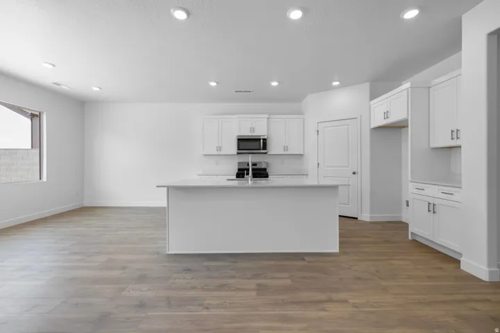 Modern kitchen featuring white cabinetry with stainless steel appliances, a large island with seating space, recessed ceiling lighting, and wood-finish flooring throughout the open-concept layout