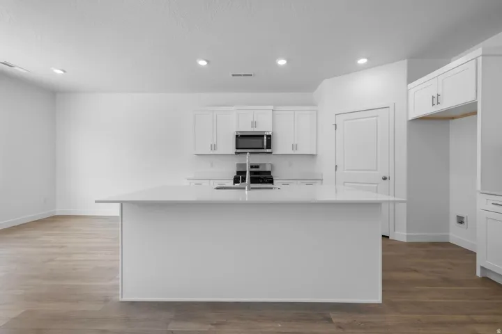 Modern kitchen featuring white cabinetry with stainless steel appliances, a large center island with waterfall countertop, recessed ceiling lighting, and wood-finish flooring throughout the open-concept space