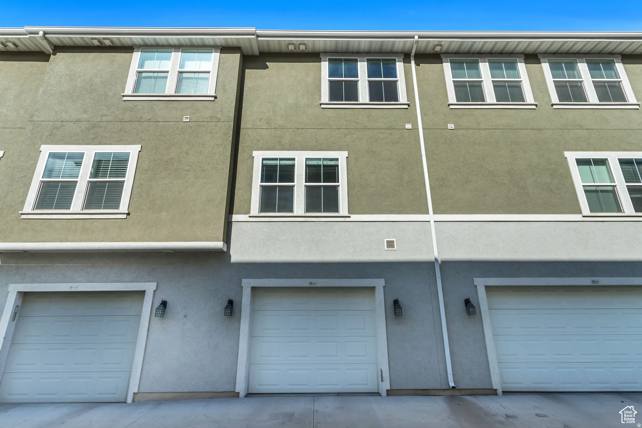 Contemporary townhome exterior featuring multi-panel windows, horizontal siding, exterior sconce lighting, and individual garage doors
