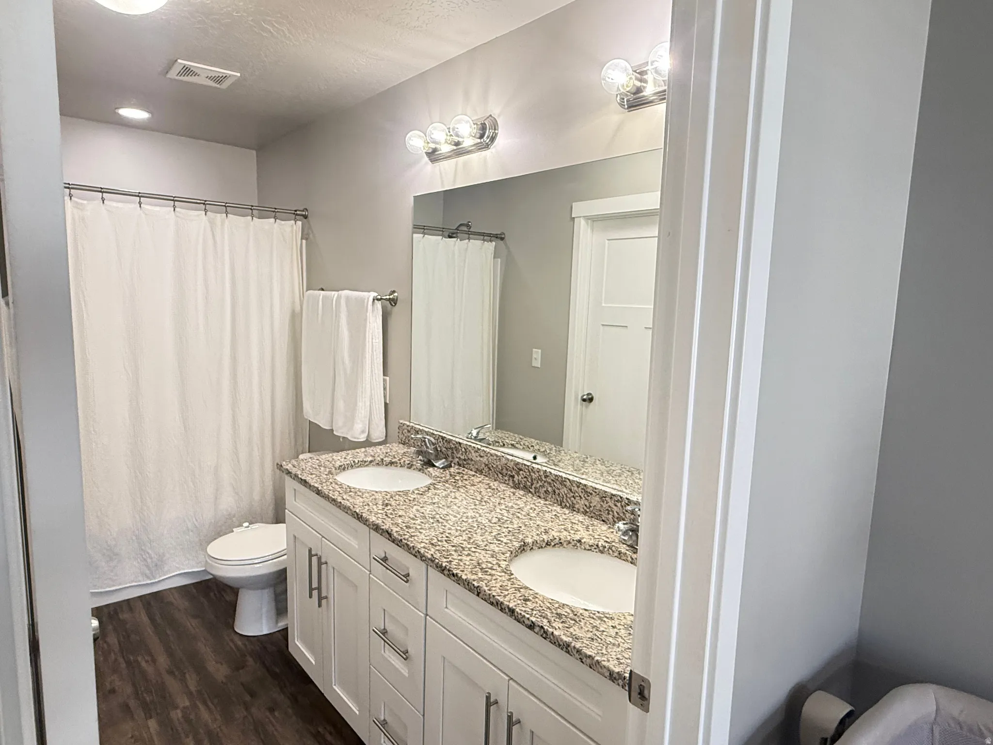 Dual-vanity bathroom featuring a granite countertop, white cabinetry with ample storage, recessed and sconce lighting, and a soaking tub with shower enclosure