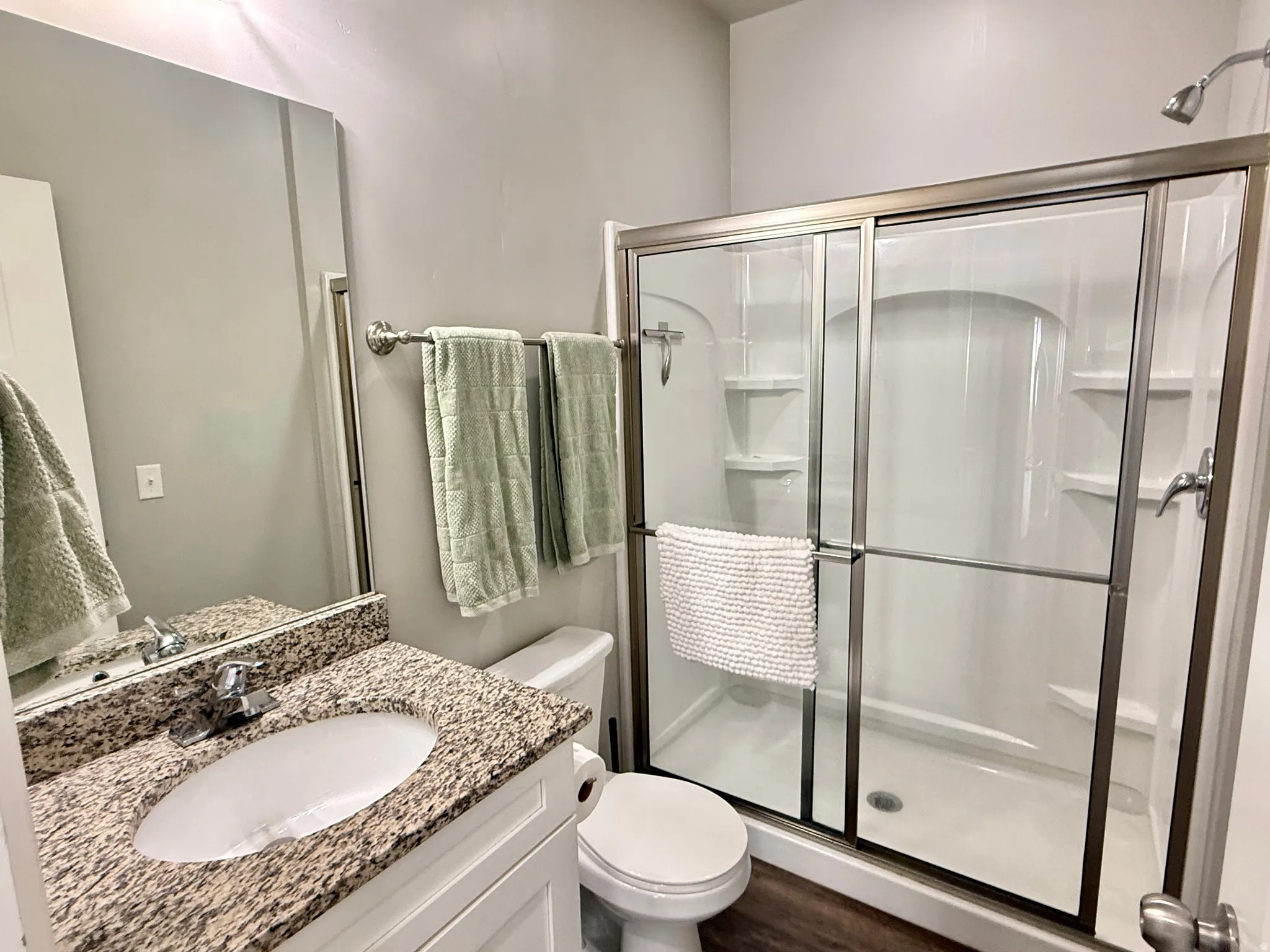 Enclosed shower with glass sliding doors, vanity with stone-finish countertop, built-in mirror, and wood-finish flooring