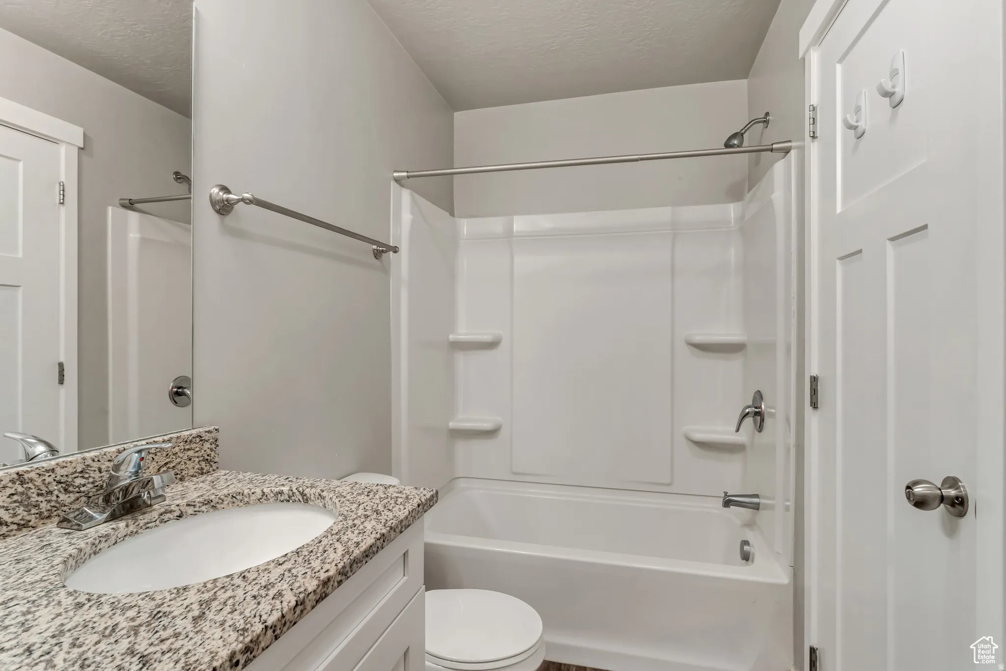 Bathroom featuring a granite-finish countertop, single basin sink, chrome faucet, white vanity, and a tub/shower combination with a white surround