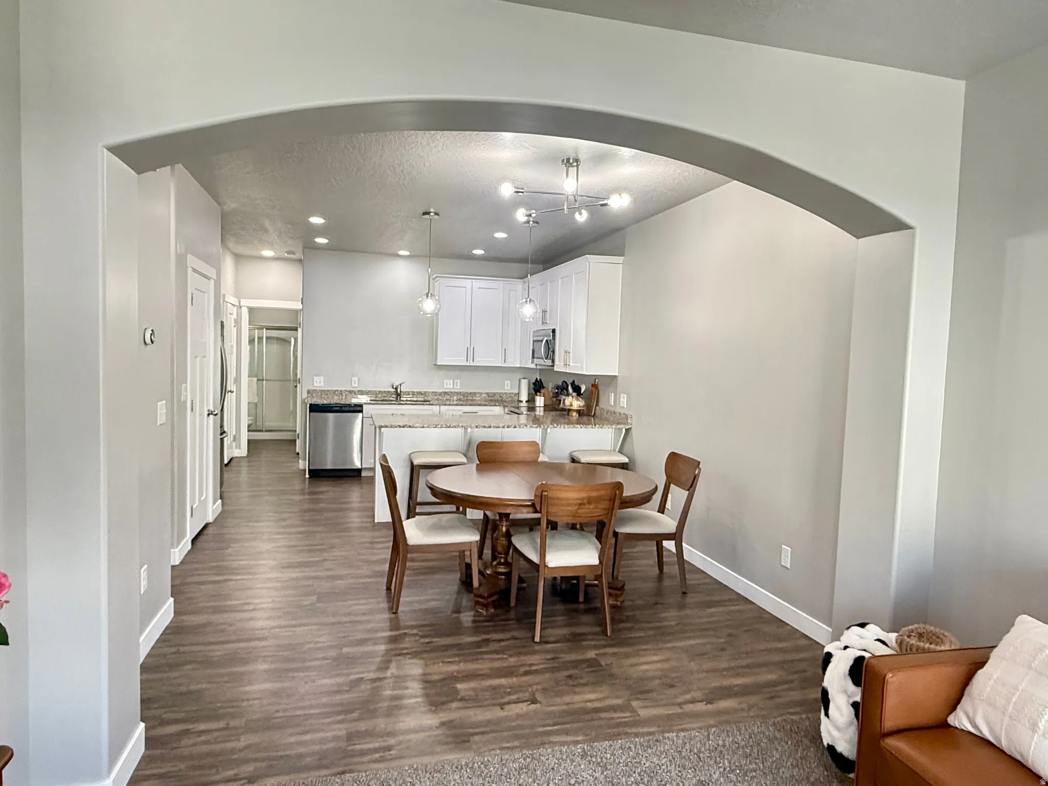 Open concept living space featuring an arched doorway, wood-finish flooring, recessed lighting, and a modern kitchen with white cabinetry and stainless steel appliances