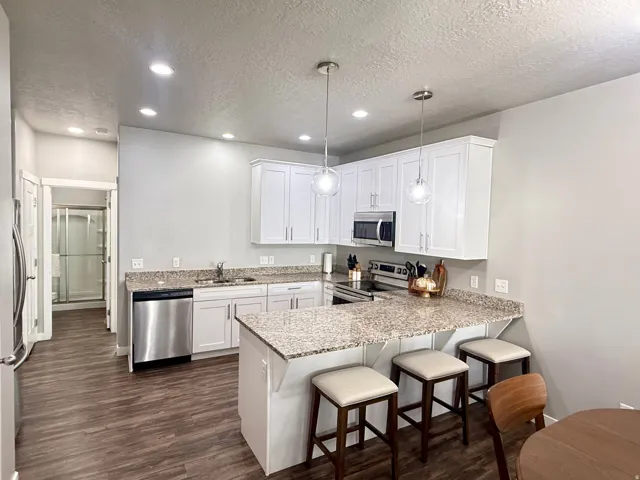 Kitchen featuring white cabinetry, stainless steel appliances, speckled stone countertops, and wood-finish flooring