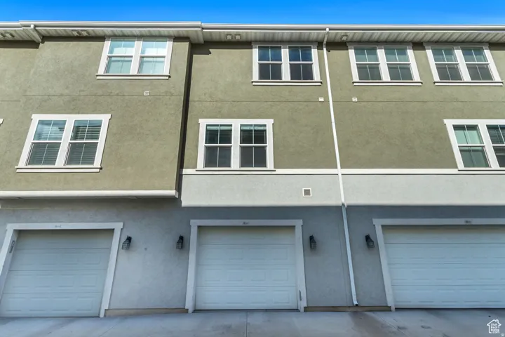 Contemporary townhome exterior featuring multi-panel windows, horizontal siding, exterior sconce lighting, and individual garage doors