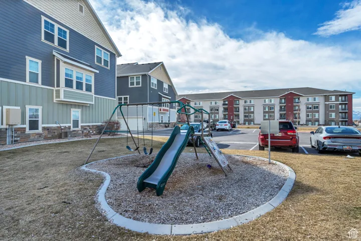 Outdoor play area with a swing set and slide, surrounded by wood chips and concrete curbing