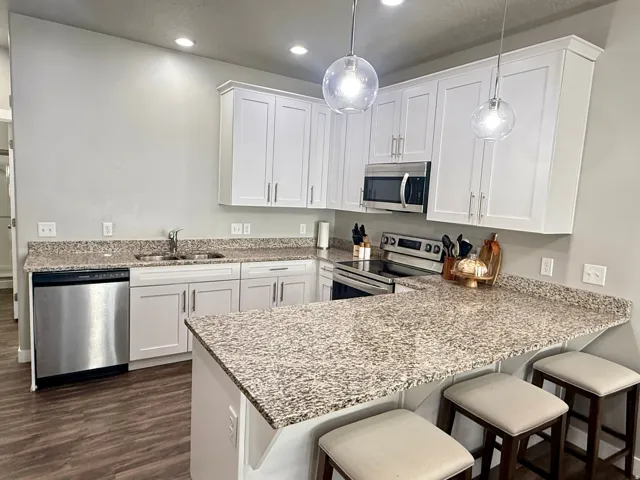 Kitchen featuring white shaker-style cabinetry, stainless steel appliances, granite countertops, and wood-finish flooring