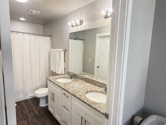 Dual-vanity bathroom featuring a granite countertop, white cabinetry with ample storage, recessed and sconce lighting, and a soaking tub with shower enclosure