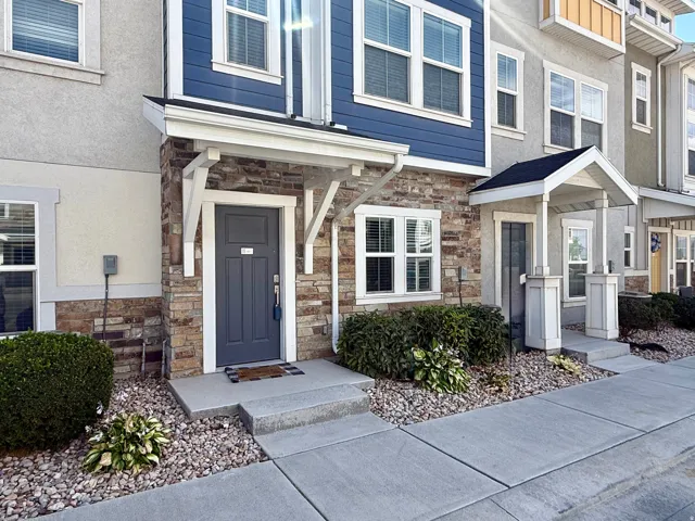Stone veneer facade with blue siding accents, covered entry, white window trim, and concrete walkway