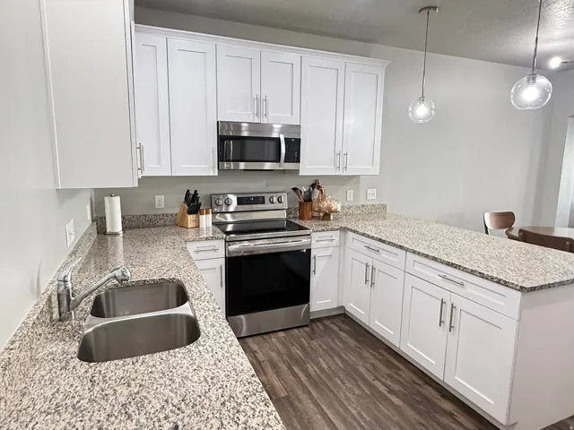 Contemporary kitchen featuring white cabinetry, granite countertops, stainless steel appliances, wood-finish flooring, and pendant lighting