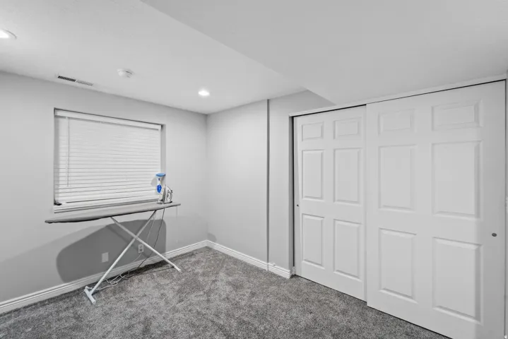Dedicated laundry room featuring neutral carpet flooring, a window with horizontal blinds, white six-panel closet doors, and recessed ceiling lighting