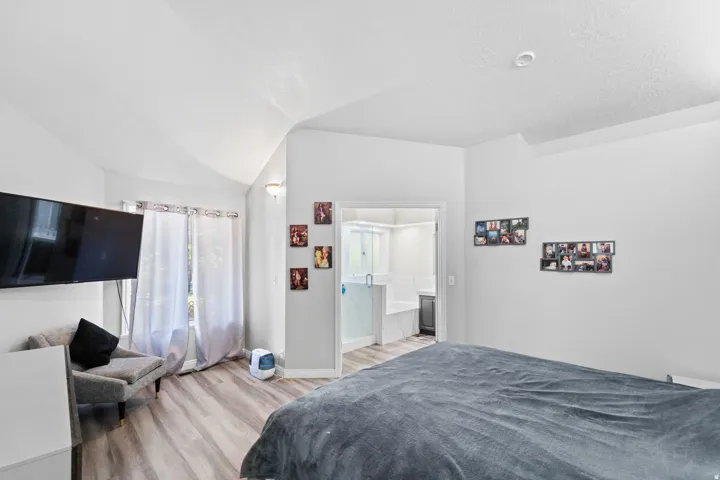 Vaulted ceiling, wood-finish flooring, recessed lighting, double window, and an adjacent bathroom with a built-in tub