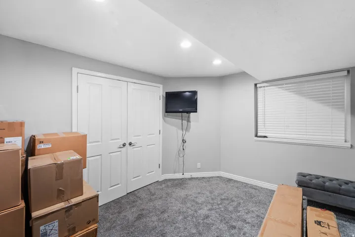 Recessed ceiling lighting, gray carpeting, neutral wall color, white window blinds, and a built-in closet with bifold doors