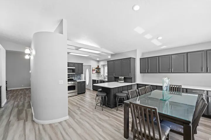 Wood-finish flooring, recessed lighting, dark cabinetry, stainless steel appliances, and a kitchen island with seating