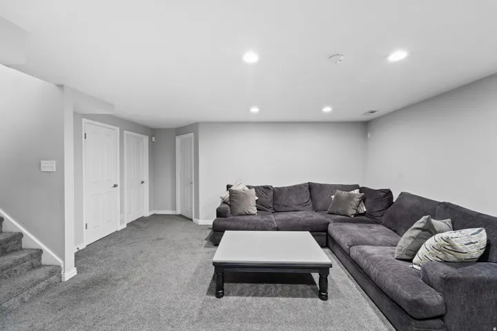 Recessed lighting illuminates the carpeted flooring and light grey wall finishes
