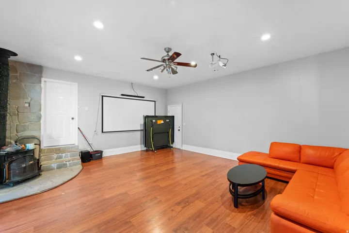 Recessed ceiling lighting, wood-finish flooring, ceiling fan, stone-clad wood-burning stove, and a wall-mounted projection screen