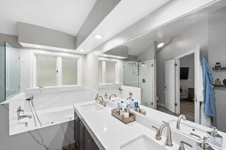 Bathroom featuring a built-in tub, dual vanities with integrated sinks, a glass-enclosed shower, and a large mirror