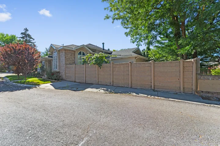 Exterior showcasing a decorative arched window, stone and stucco facade, a mature deciduous tree, and a concrete perimeter fence