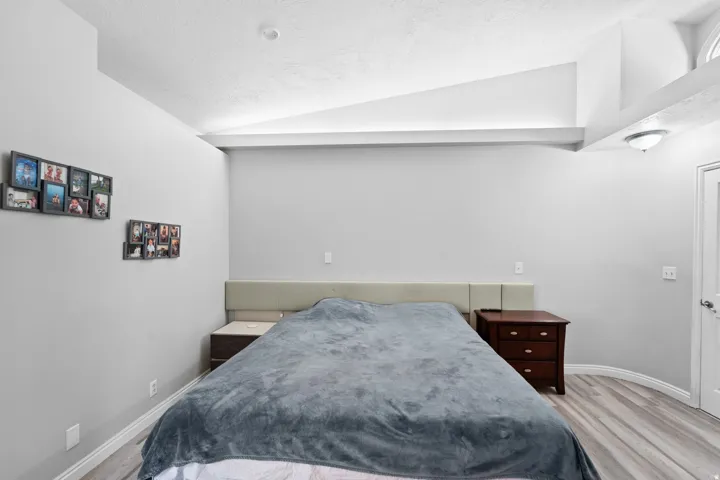 Vaulted ceiling with architectural beams, wood-finish flooring, and white trim