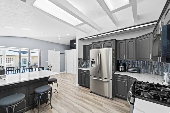 Wood-finish flooring, vaulted ceilings with exposed beams, recessed lighting, and a kitchen island with a quartz countertop