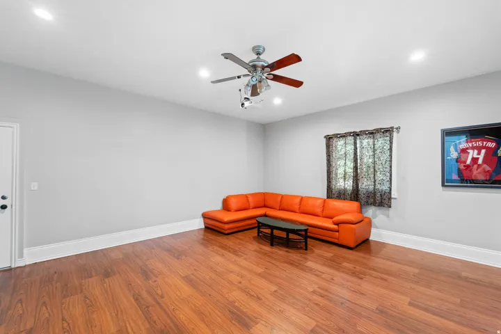 Wood-finish flooring, recessed lighting, ceiling fan with light, and window with dark patterned drapes