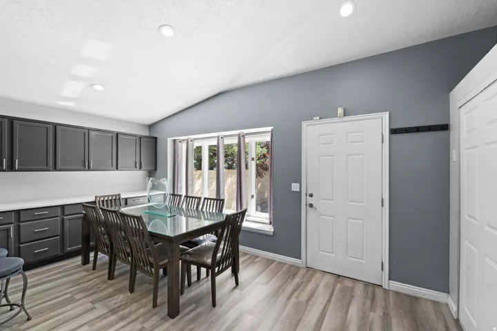 Vaulted ceiling with recessed lighting, wood-finish flooring, dark-toned cabinetry with light countertops, and a white paneled door