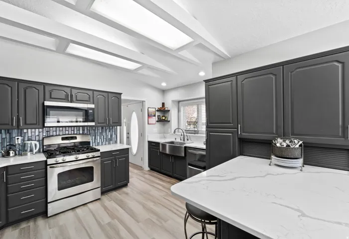 Kitchen featuring dark cabinetry, white quartz countertops, stainless steel appliances, a tiled backsplash, and wood-finish flooring