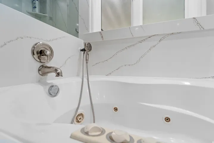 White jetted tub featuring a deck-mounted faucet and handheld shower sprayer