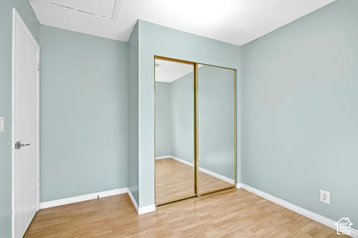 Bedroom 3. Wood-finish flooring, light blue wall paint, mirrored closet doors, and a white interior door with contemporary hardware