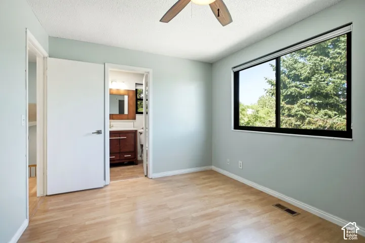 Master bedroom with door into main bathroom. Wood-finish flooring, ceiling fan, and large window with natural light