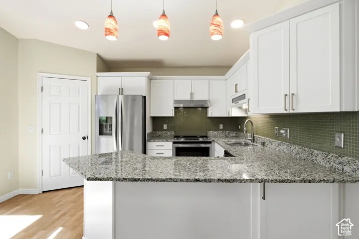Kitchen featuring white cabinetry, light-toned countertops, stainless steel appliances, a tile backsplash, and wood-finish flooring